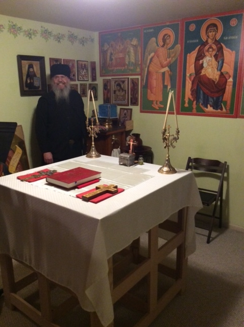 The altar table with a temporary covering, and with
    the Gospel, cross and other items on it. Father Symeon, the parish priest, is in the
    background.
