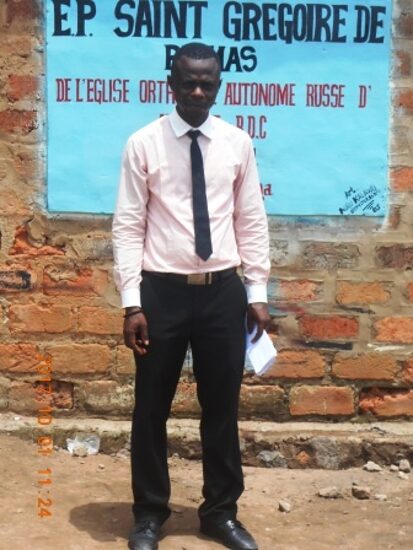 A teacher in front of the sign of the Saint Gregory Palamas primary school