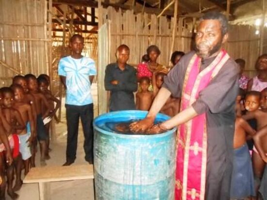 A priest in an epitrachelion baptizing a child by immersion in a barrel font