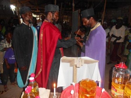 Priests in vestments anointing the faithful at the Holy Unction, bottles of oil on the table