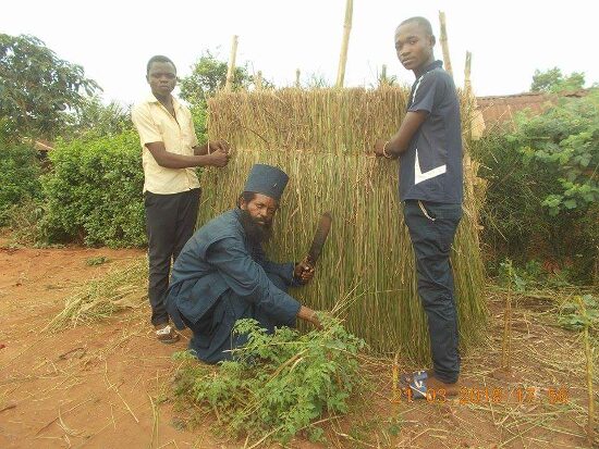 Father Theophile and two young men building a wall of bundled grass