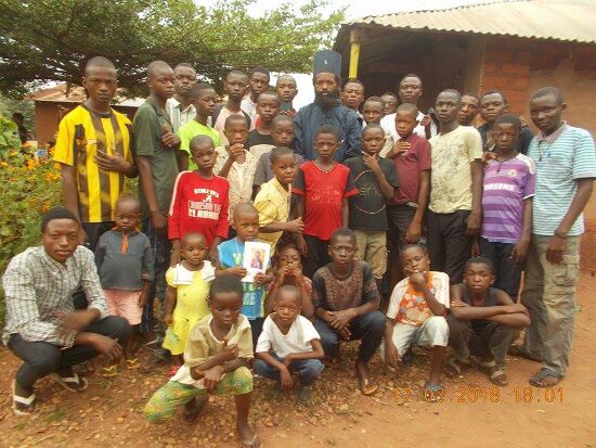 A large group of young people and children of the parish outdoors, Father Theophile among them