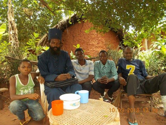Father Theophile sitting outdoors with young men of the parish around a small table