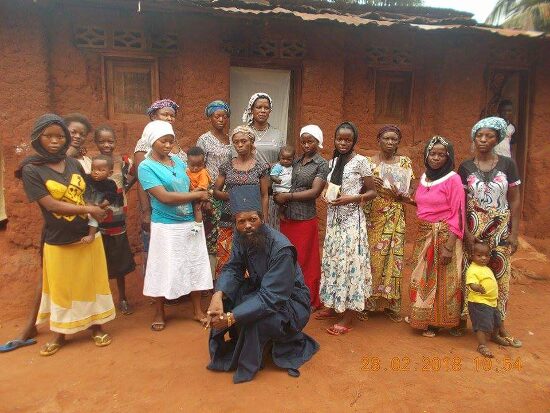 Father Theophile kneeling in front of a group of women and children of the parish