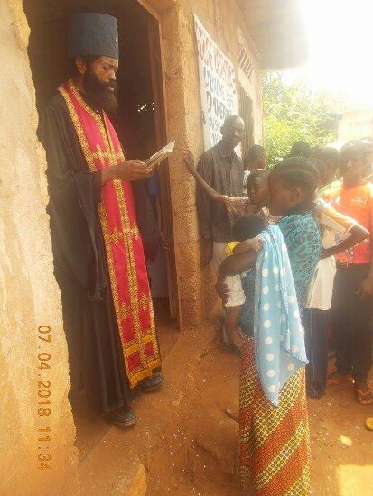 Father Theophile in an epitrachelion reading a prayer at the door of the church, the faithful outside