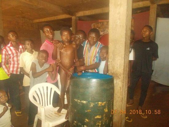 Father Theophile baptizing by immersion in a large barrel font, the faithful looking on