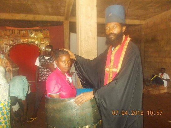 Father Theophile baptizing by immersion in a large barrel font, the faithful looking on