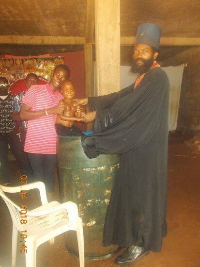 Father Theophile baptizing by immersion in a large barrel font, the faithful looking on