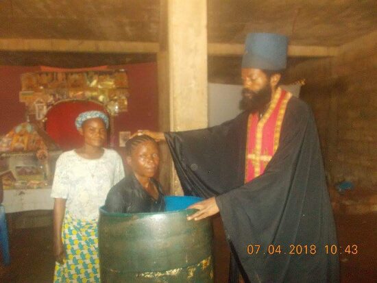Father Theophile baptizing by immersion in a large barrel font, the faithful looking on