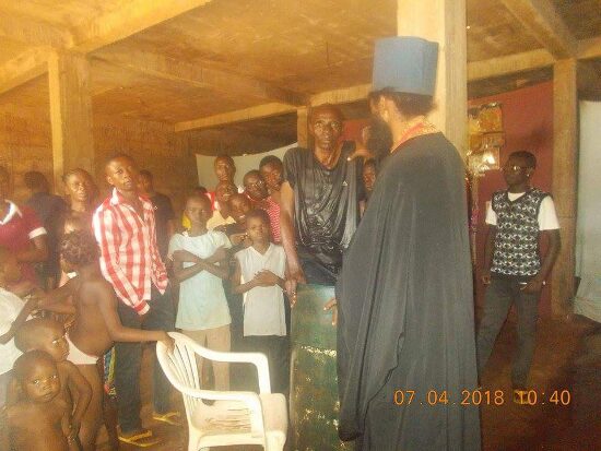 Father Theophile baptizing by immersion in a large barrel font, the faithful looking on
