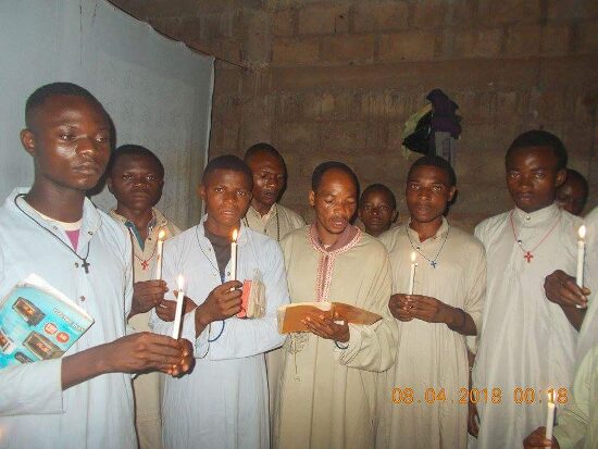 Young men in white robes holding candles by night