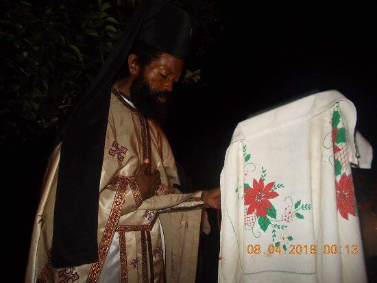 Father Theophile in vestments by night beside a lectern covered with an embroidered cloth