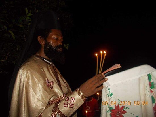 Father Theophile reading by candlelight at a lectern outside, the start of the Paschal service