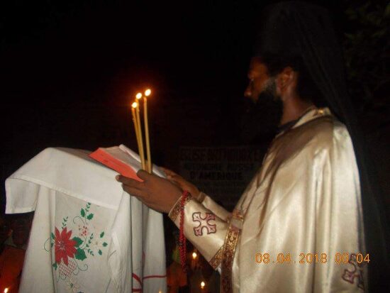 Father Theophile reading by candlelight at a lectern outside, the start of the Paschal service